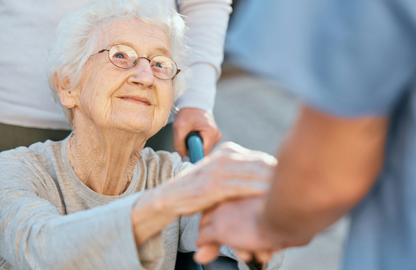 Holding hands, caregiver and senior woman in wheelchair for support outdoor in retirement home. Lov